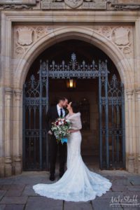 A couple kisses in front of the gates of Meadow Brook Hall on their wedding day.