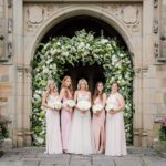 Bride and Bridesmaids pose outside Meadow Brook Hall's front gates, decorated with a flower arch.