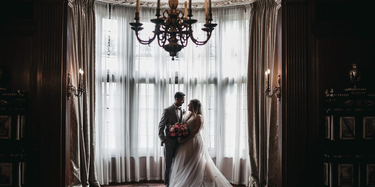 Bride and Groom in front of elegant historic window and chandelier.