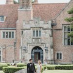 Young couple holds hands on their wedding day in front of the gates of Meadow Brook Hall.