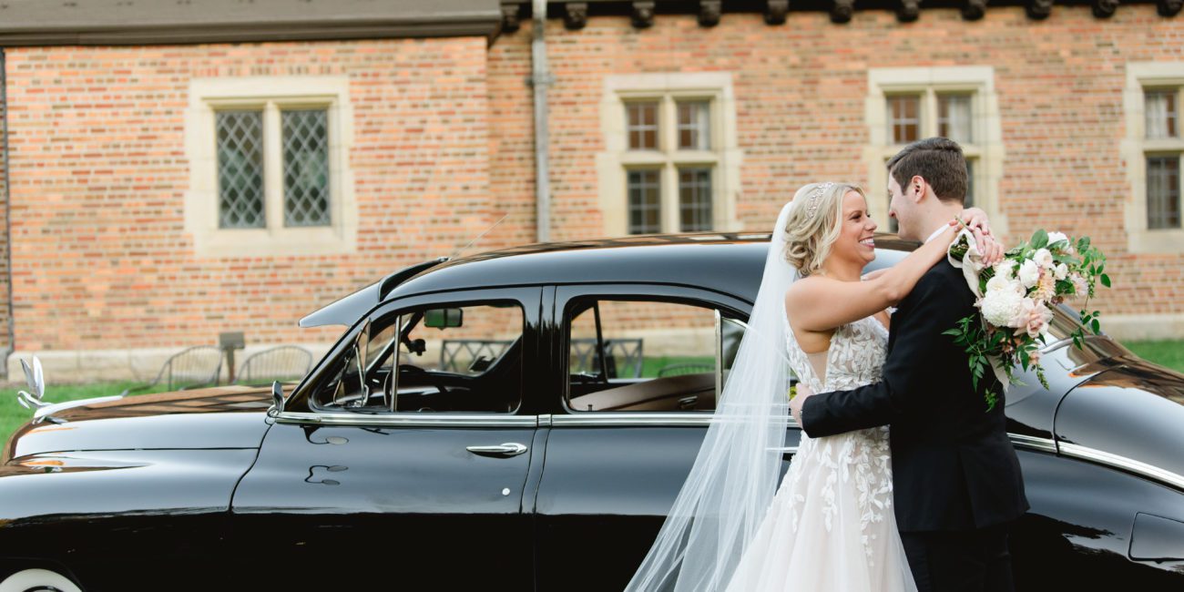 Newly married couple kisses next to a vintage car at Meadow Brook Hall