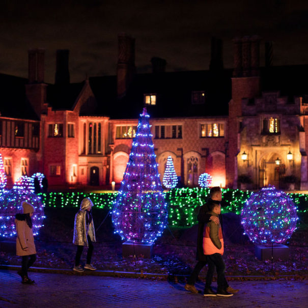 A group of adults and children walk past brilliantly lighted decorations with Meadow Brook Hall in the background