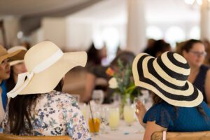 Two women in floppy hats enjoy the Champagne Garden Party at Meadow Brook